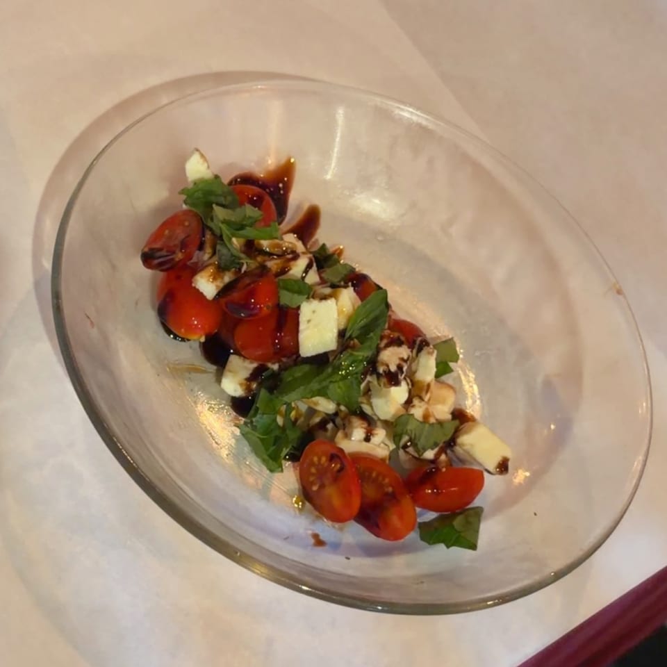 Caprese salad with cherry tomatoes, mozzarella, basil, and balsamic glaze in a clear dish.