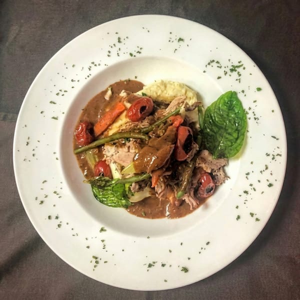 Braised meat with gravy, roasted vegetables, and mashed potatoes on a white plate.