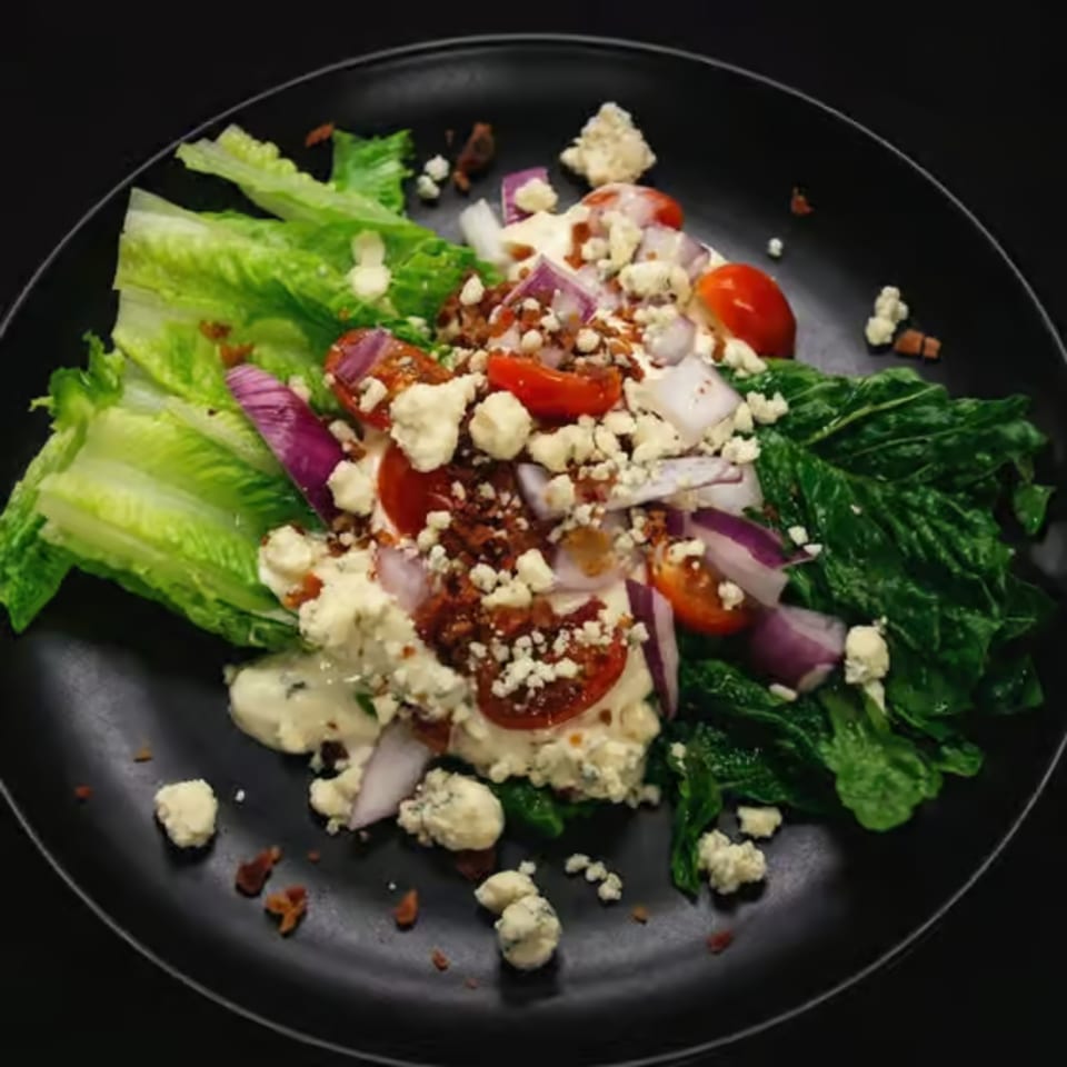 Wedge salad with blue cheese, bacon, red onion, and cherry tomatoes on a black plate.